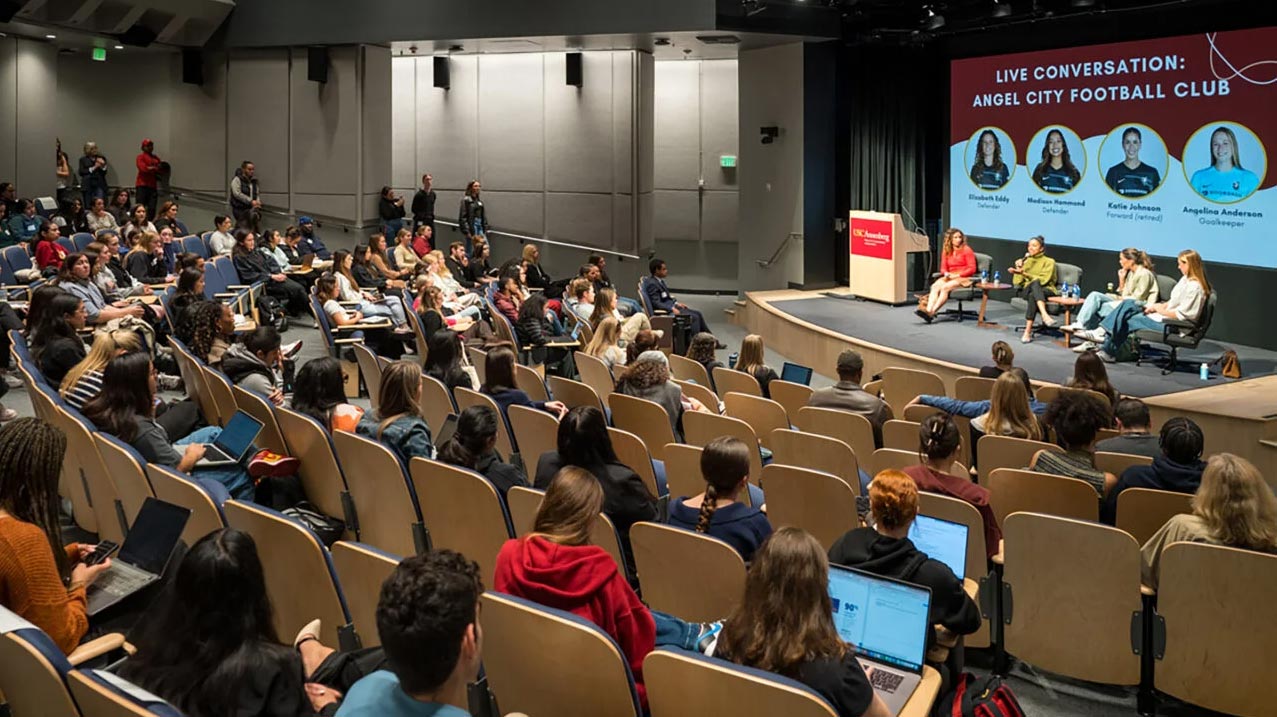 A full auditorium watches a panel of four women soccer players.